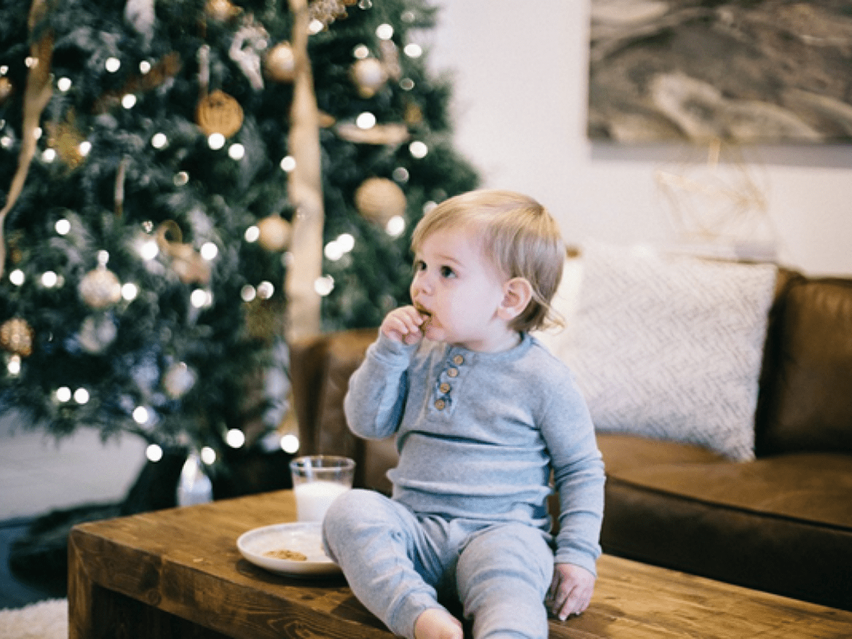 Young child sitting on a wooden table with hand in mouth, Christmas tree in the background