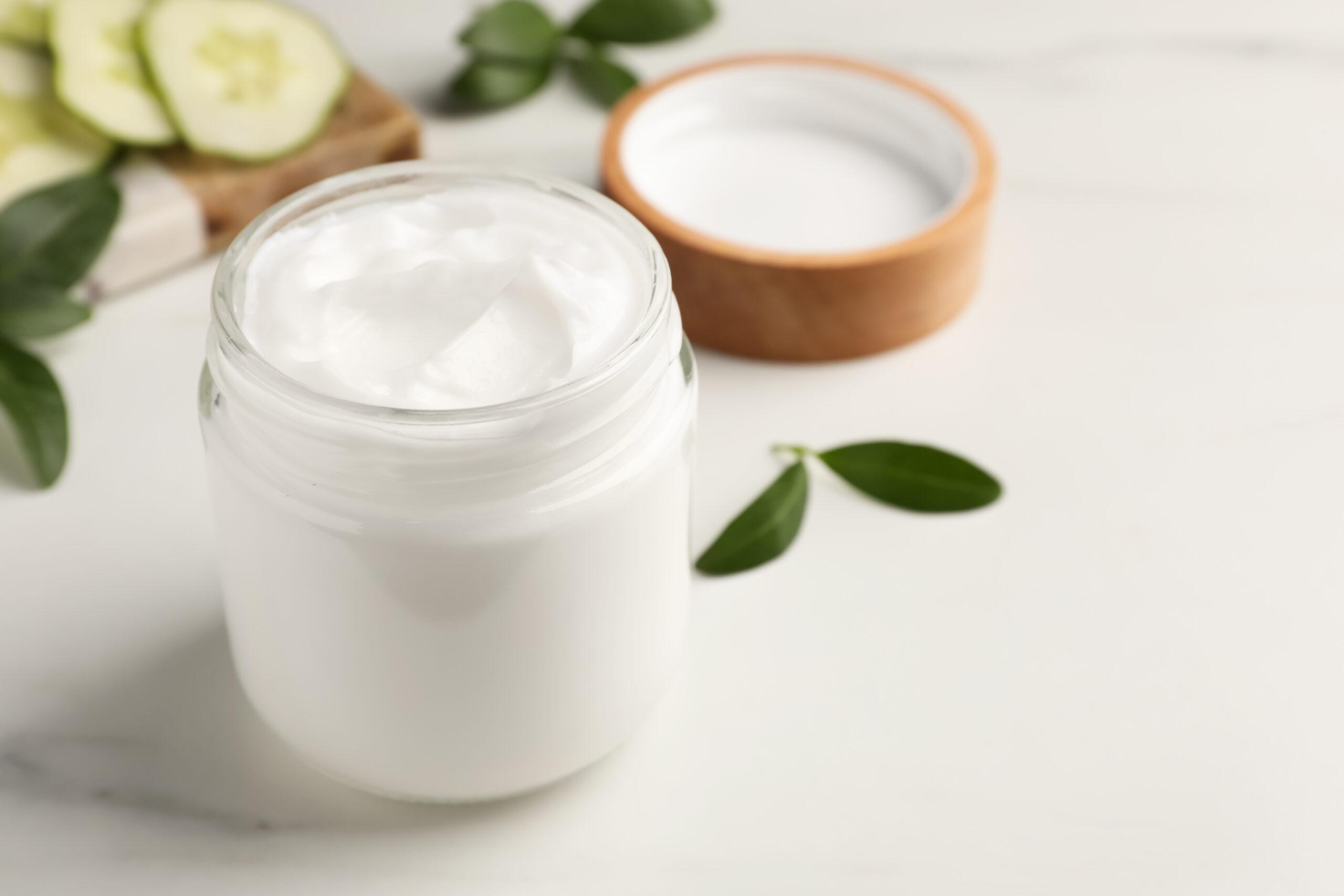 Glass jar of face cream on white marble table. Space for text